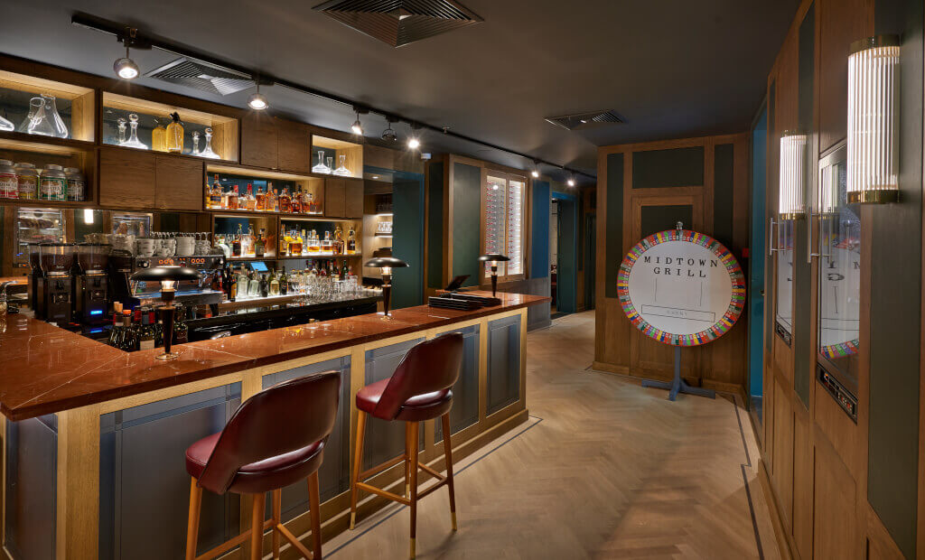 De sfeervolle bar van Restaurant Midtown Grill in Gent met een visgraatmotief parketvloer en donkerrode op maat gemaakte zitmeubels.